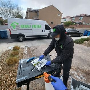 Technician in black uniform packages a device on a cart beside a white service van in a suburban driveway