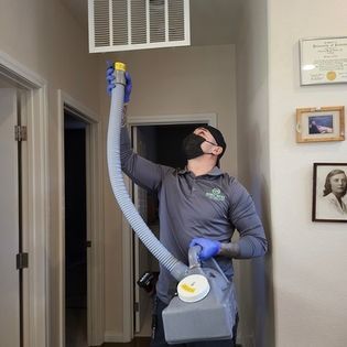 Technician disinfecting a hallway air vent with a spray machine indoors