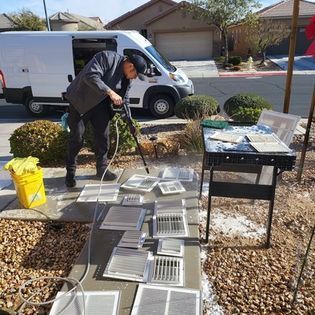 Worker inspecting vents at a driveway display beside a white van and tools