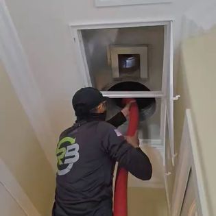 Worker using a red hose to clean a ceiling vent from a stairwell opening