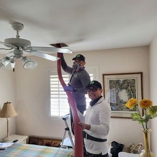 Two people changing a ceiling fan light bulb in a bright living room