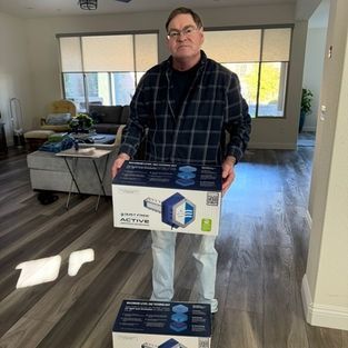 Man holding a box in a bright living room, with another box on the floor in front of him