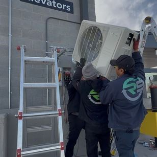 Workers lifting a large outdoor air conditioner unit beside a ladder in an industrial setting