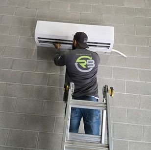 Technician on a ladder servicing a wall-mounted air conditioner
