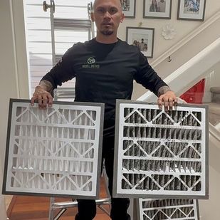 Man holding two framed air filters indoors, one white and one dark gray.