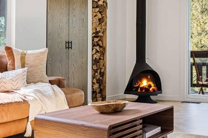 Cozy living room with a modern fireplace, wood coffee table, and sofa beside tall windows