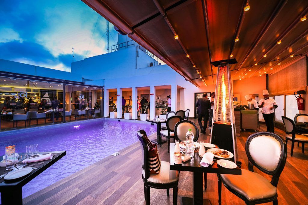 Modern outdoor patio dining area beside a lit pool at sunset