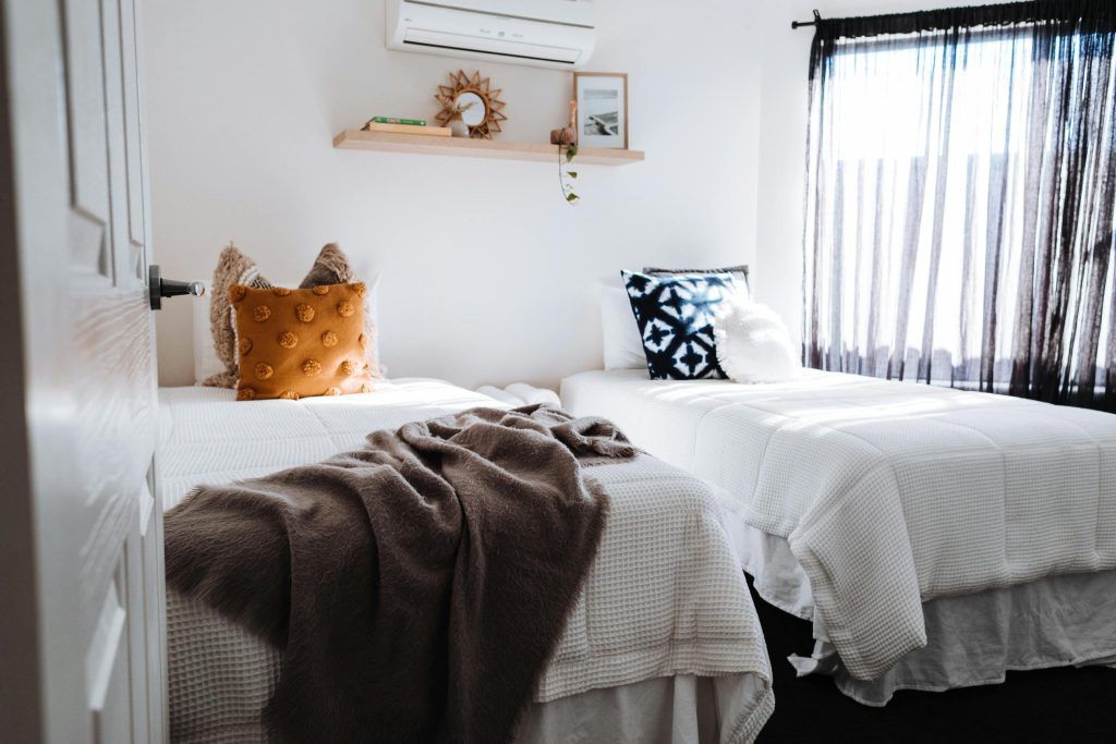 Bright bedroom with two white beds, brown throw blanket, and a window with dark curtains