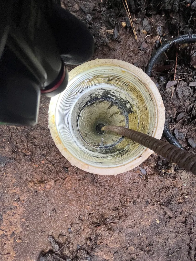 A high-angle shot looking down into a light-colored pipe in the dirt, with a dark hose running into the center.