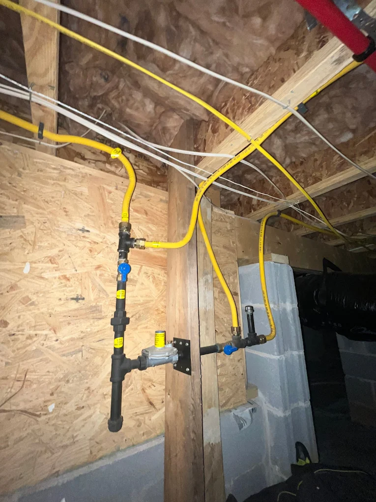 Yellow CSST gas pipes connected to black iron pipe fittings and a pressure regulator mounted on a wooden basement wall.
