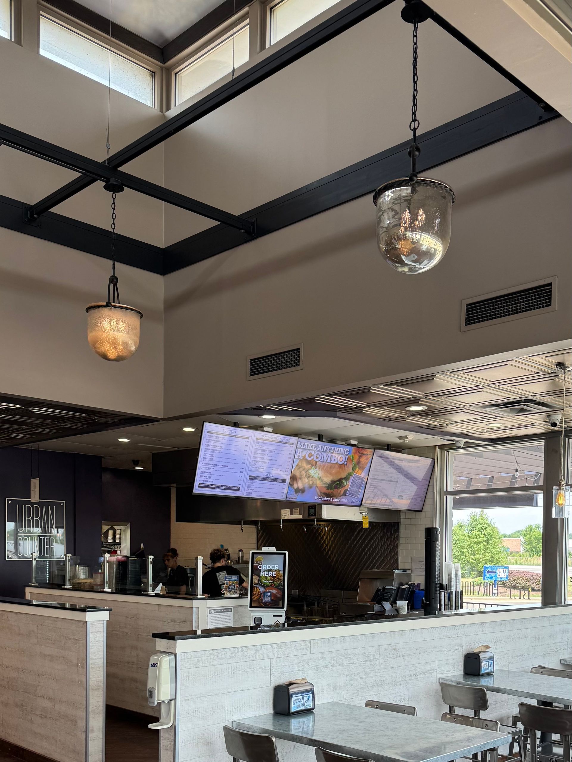 Restaurant interior with hanging lights, metal beams, and counter with a TV.