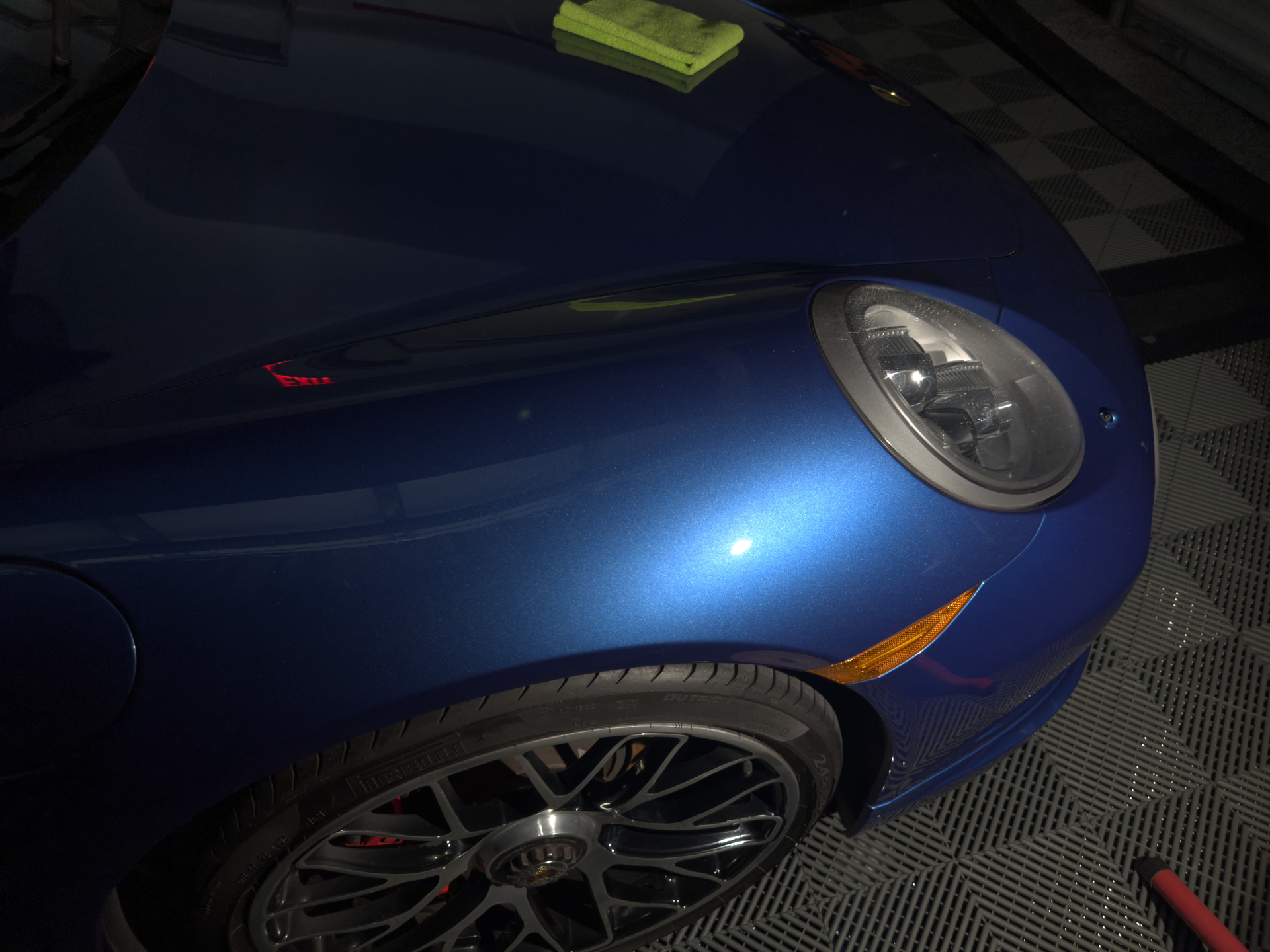 Blue sports car's front with a circular headlight, orange side marker, and alloy wheels.