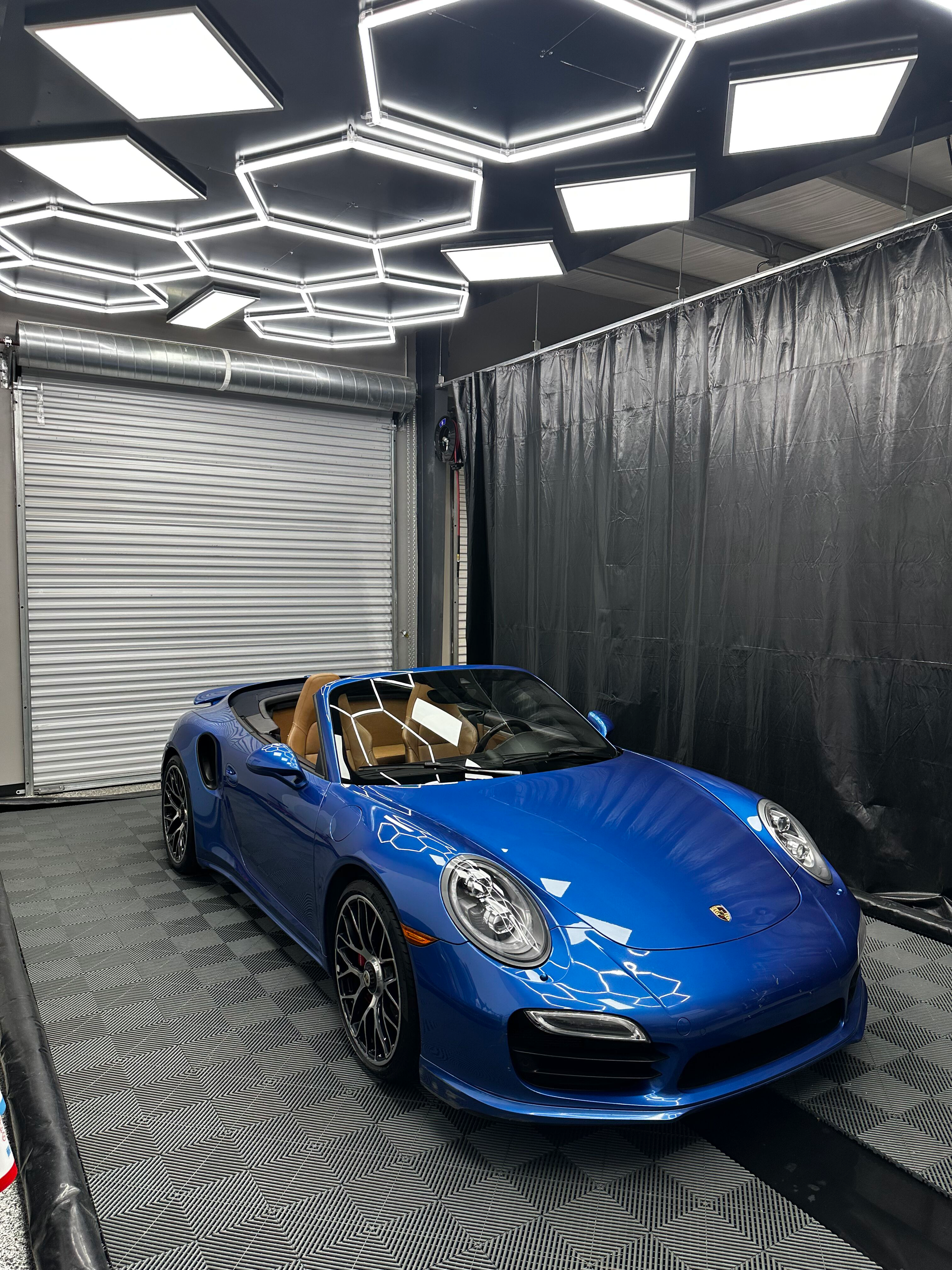 Blue Porsche convertible inside a well-lit garage, featuring hexagon lights and patterned floor.