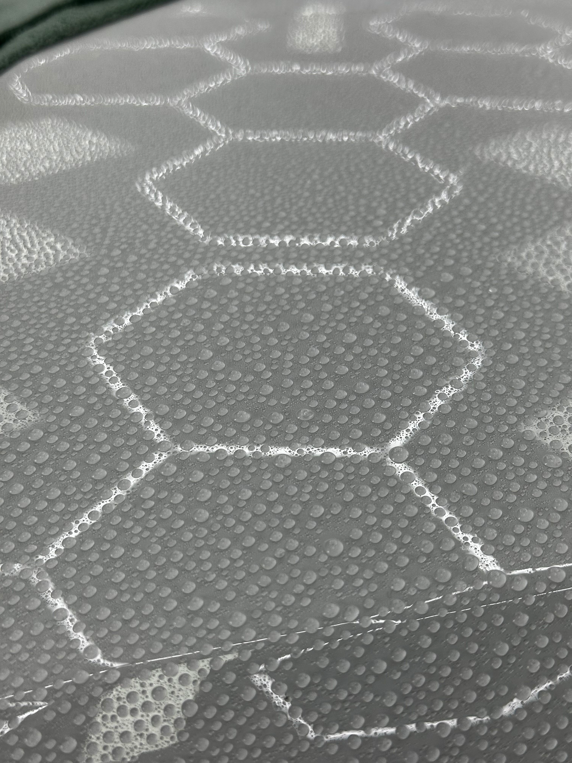 Close-up view of a white surface patterned with a repeating honeycomb design. The surface has numerous small, rounded bumps.