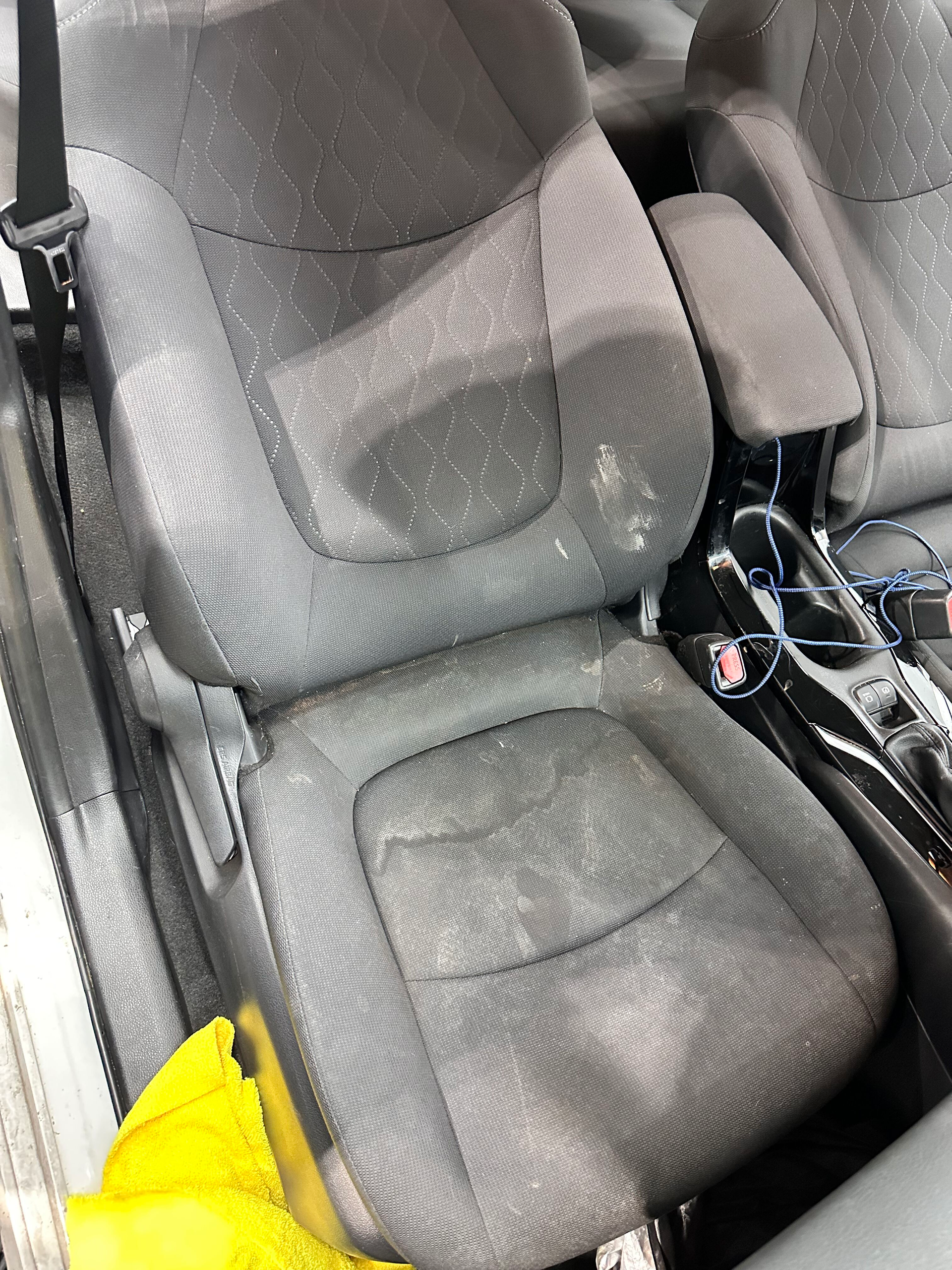 Gray fabric car seats with visible stains and debris. A yellow cloth is in the corner.