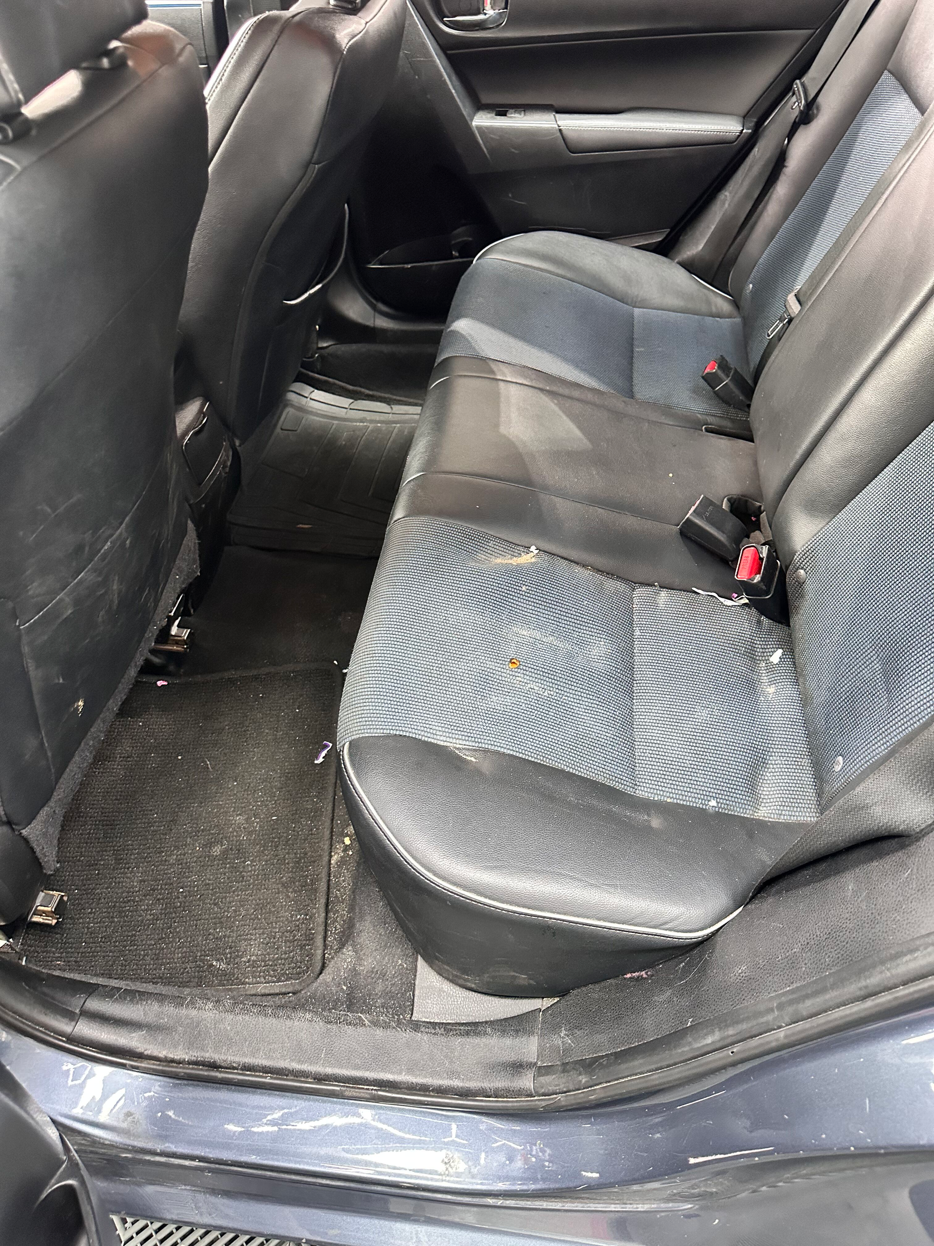 Interior view of a car's back seat. The black and blue seats are stained, with dirt and debris on the floor.