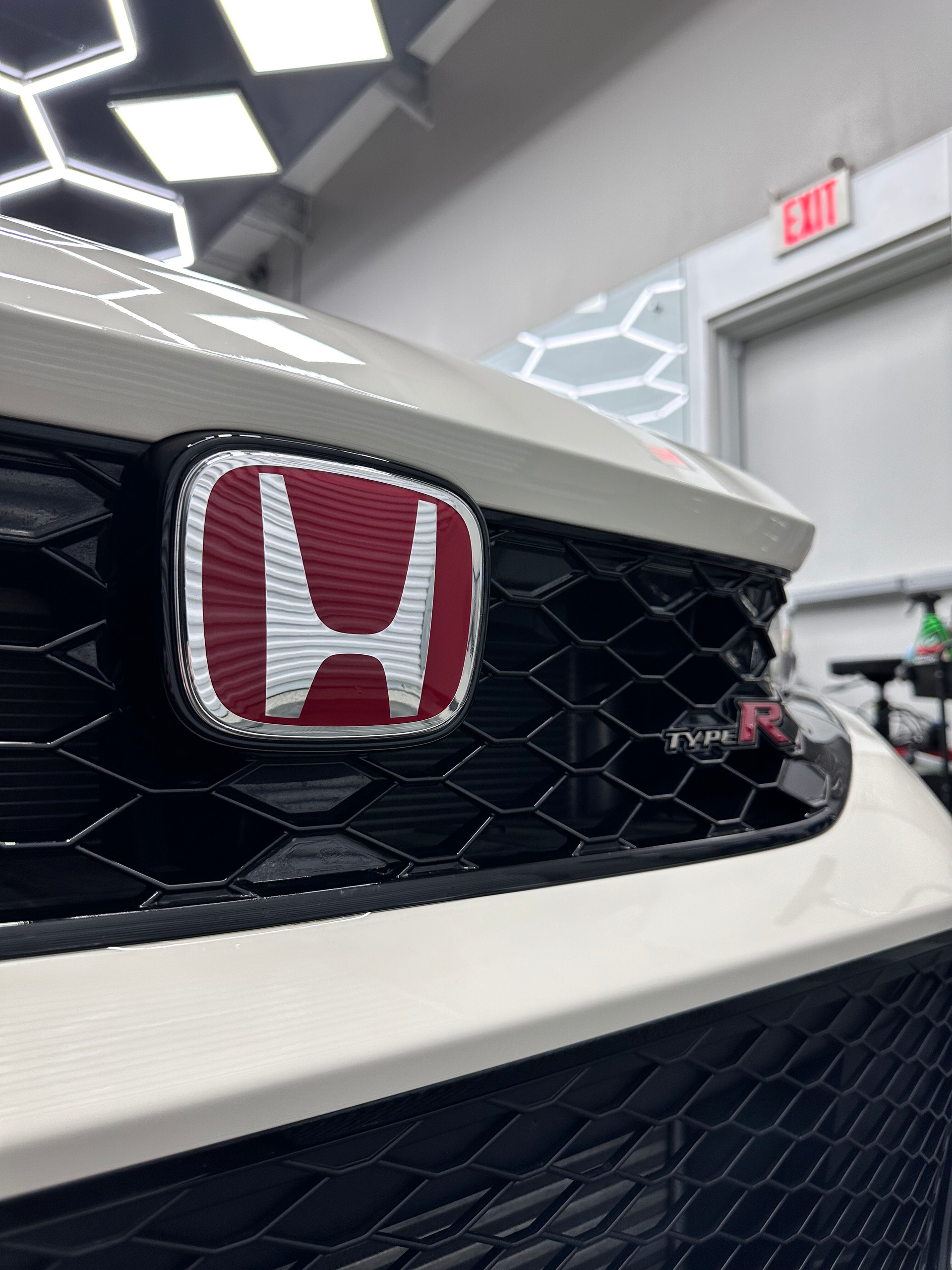 Close-up of a white Honda Type R car's front grille with a red Honda emblem.