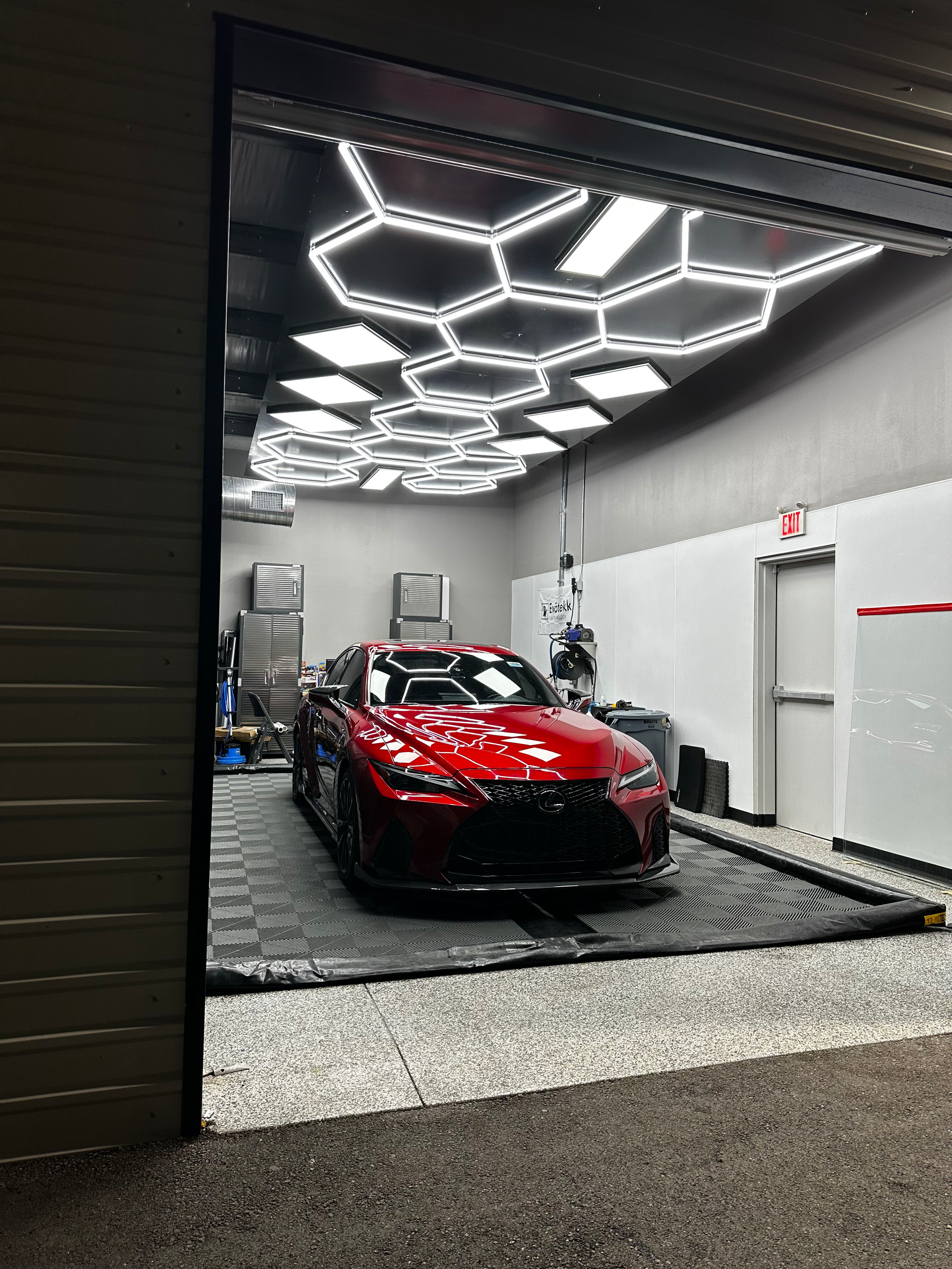 Red car inside a garage with hexagonal lights, a gray floor, and an open doorway.