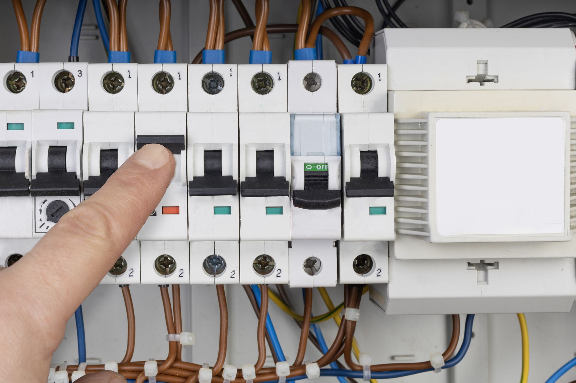 A person is pointing at a circuit breaker in an electrical box.