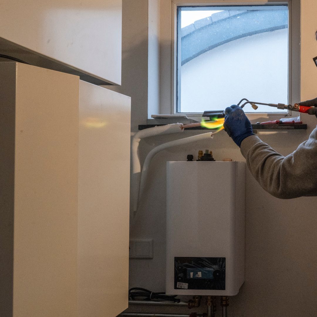 A man is working on a boiler with a screwdriver.