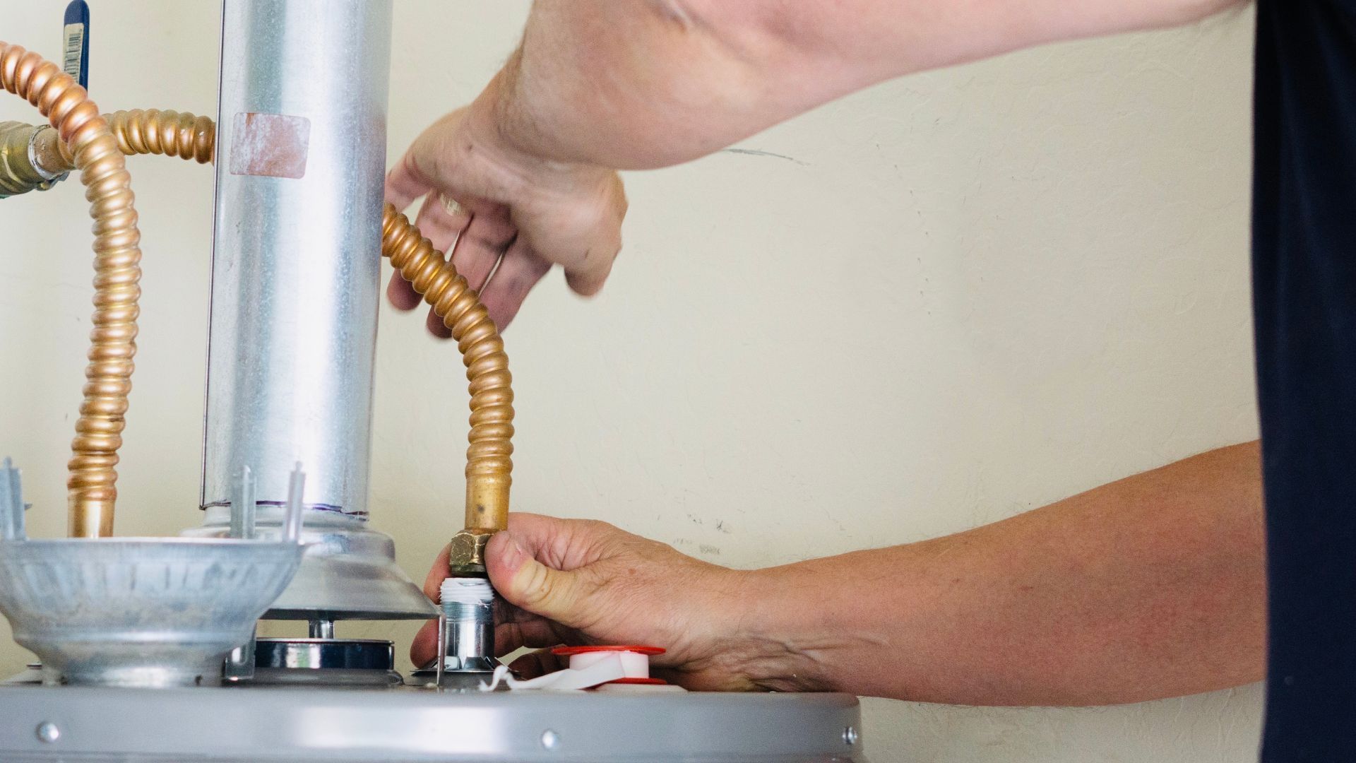 A man is fixing a water heater with a wrench.