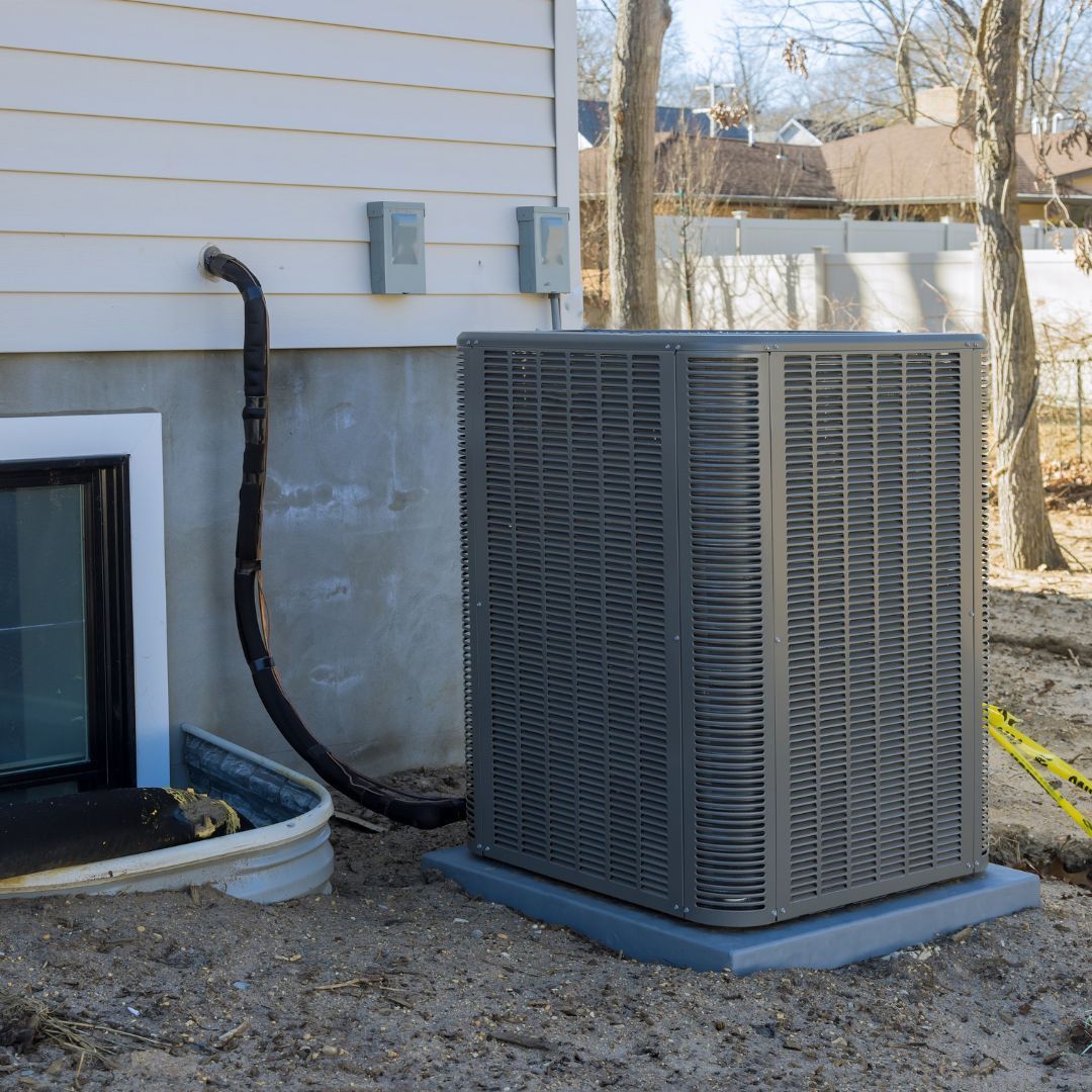 An air conditioner is sitting outside of a house next to a window.
