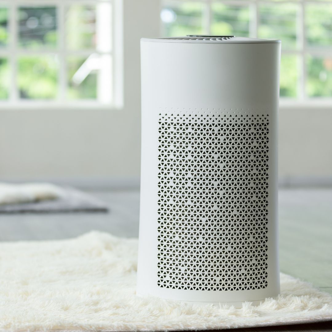 A white air purifier is sitting on a white rug in front of a window.