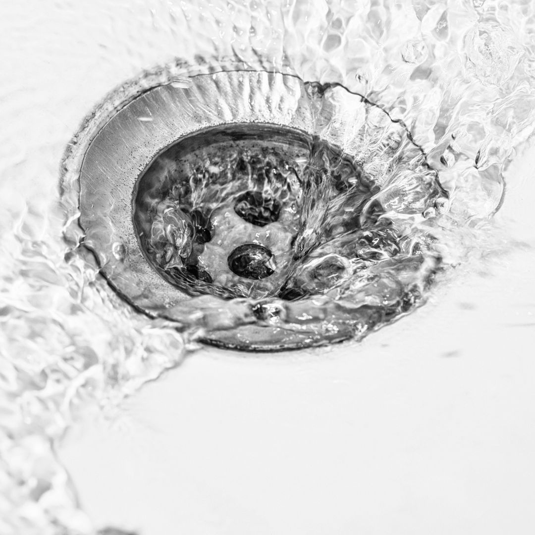 A black and white photo of water running down a sink drain.