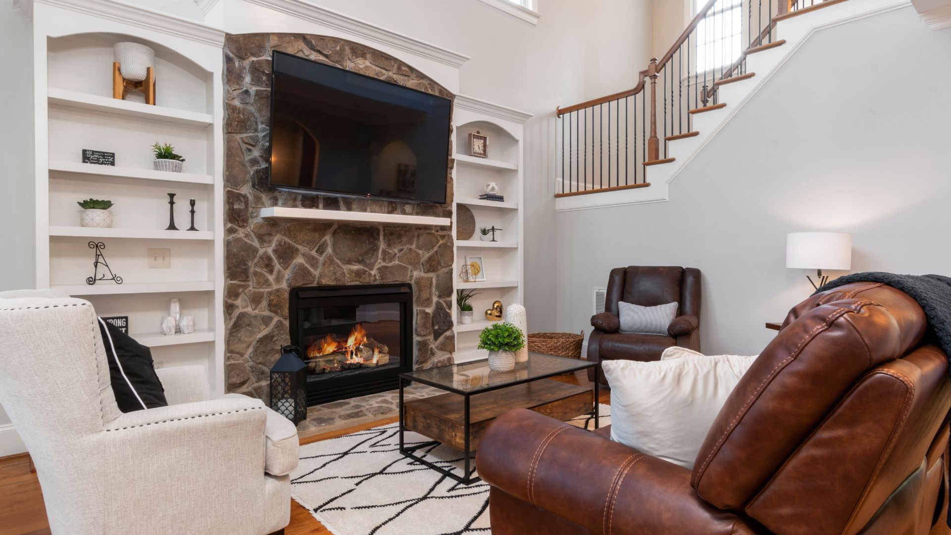 A living room with a fireplace , chairs , and a flat screen tv.
