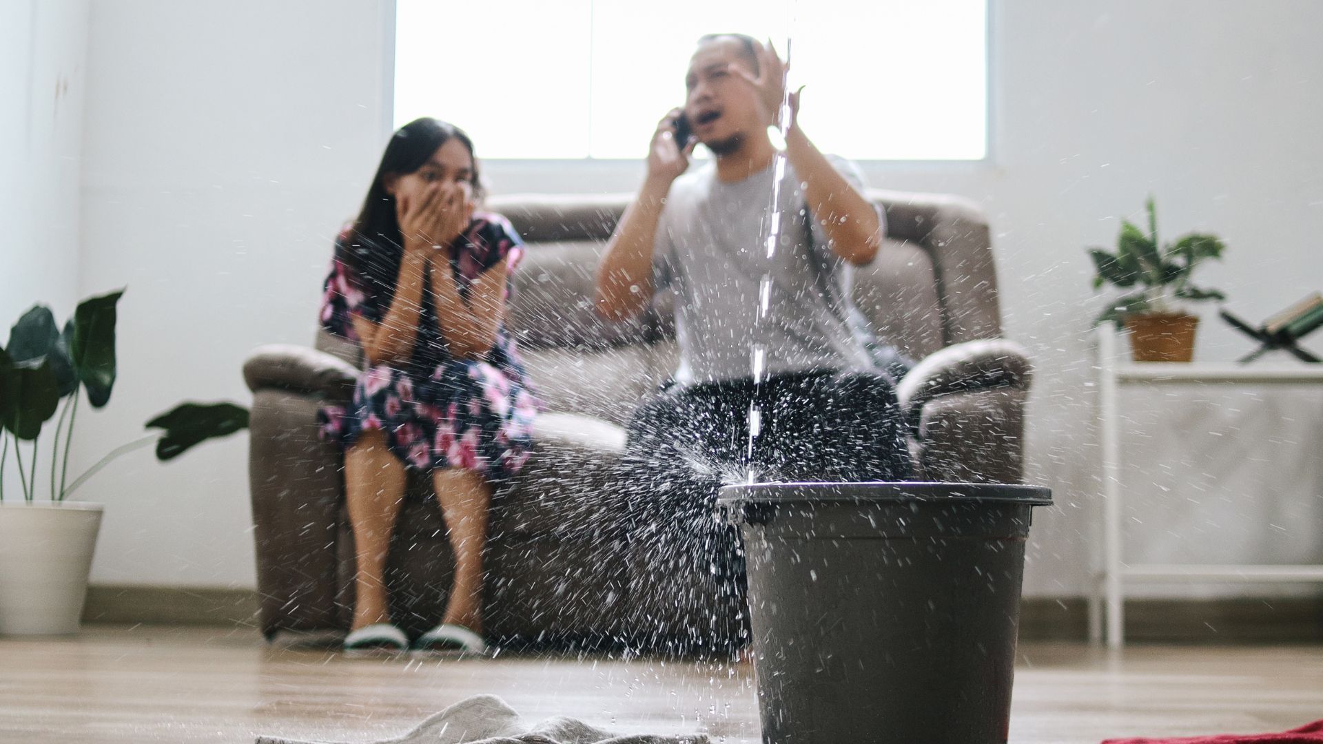 A man is talking on a cell phone while a woman sits on a couch.