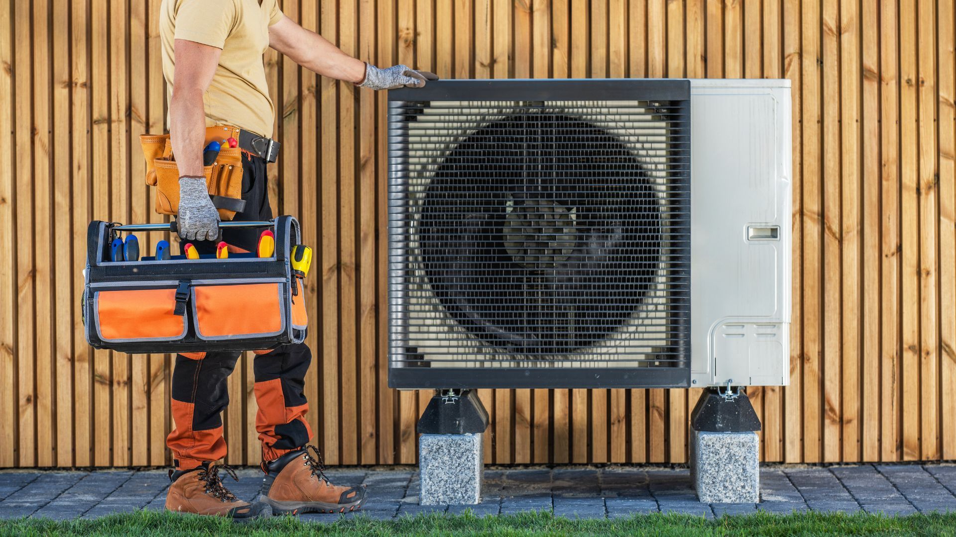 A man is holding a toolbox and working on a heat pump.