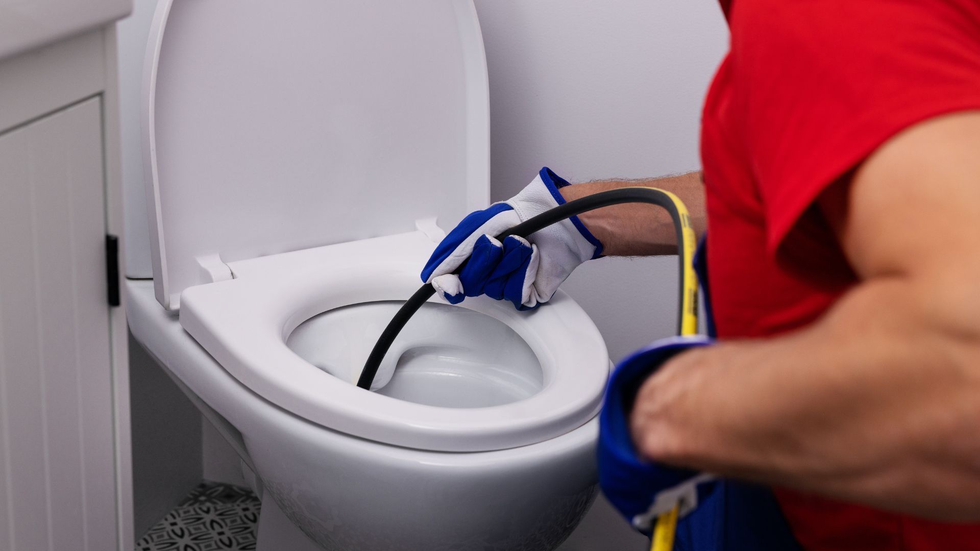 A man is cleaning a toilet with a hose.