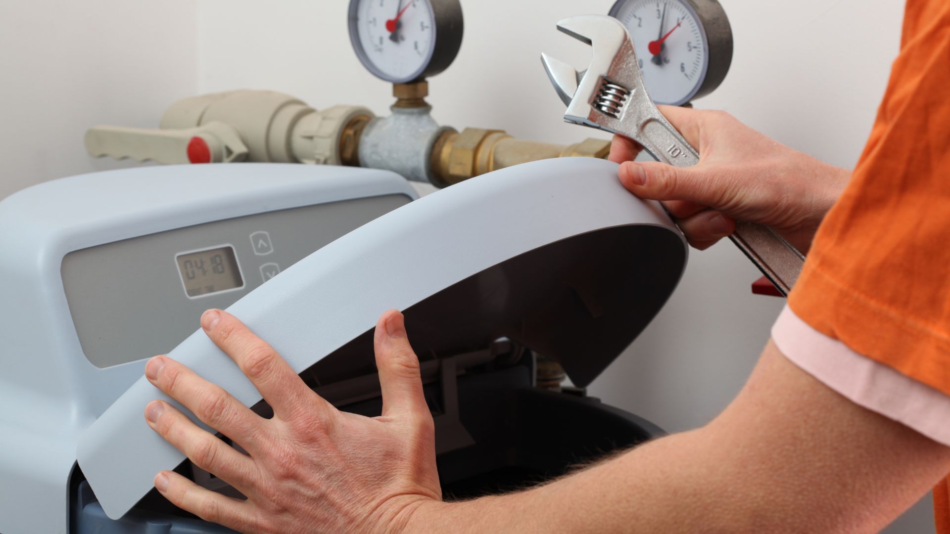 A person is fixing a water softener with a wrench.