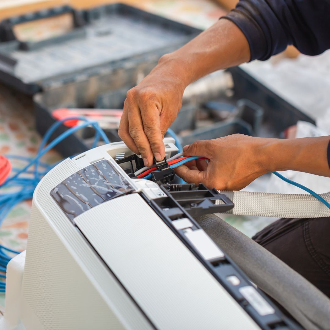 A man is fixing an air conditioner with a pair of pliers.