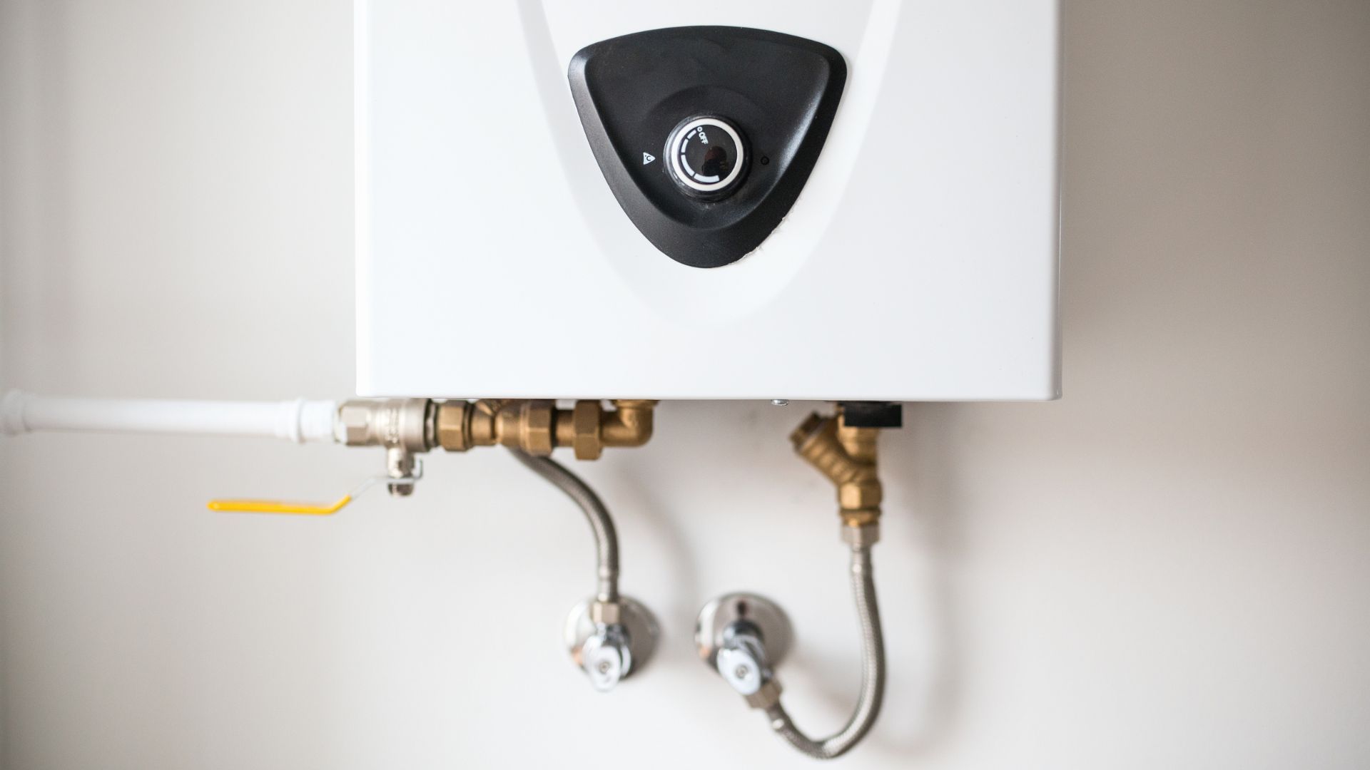 A white water heater is hanging on a white wall.