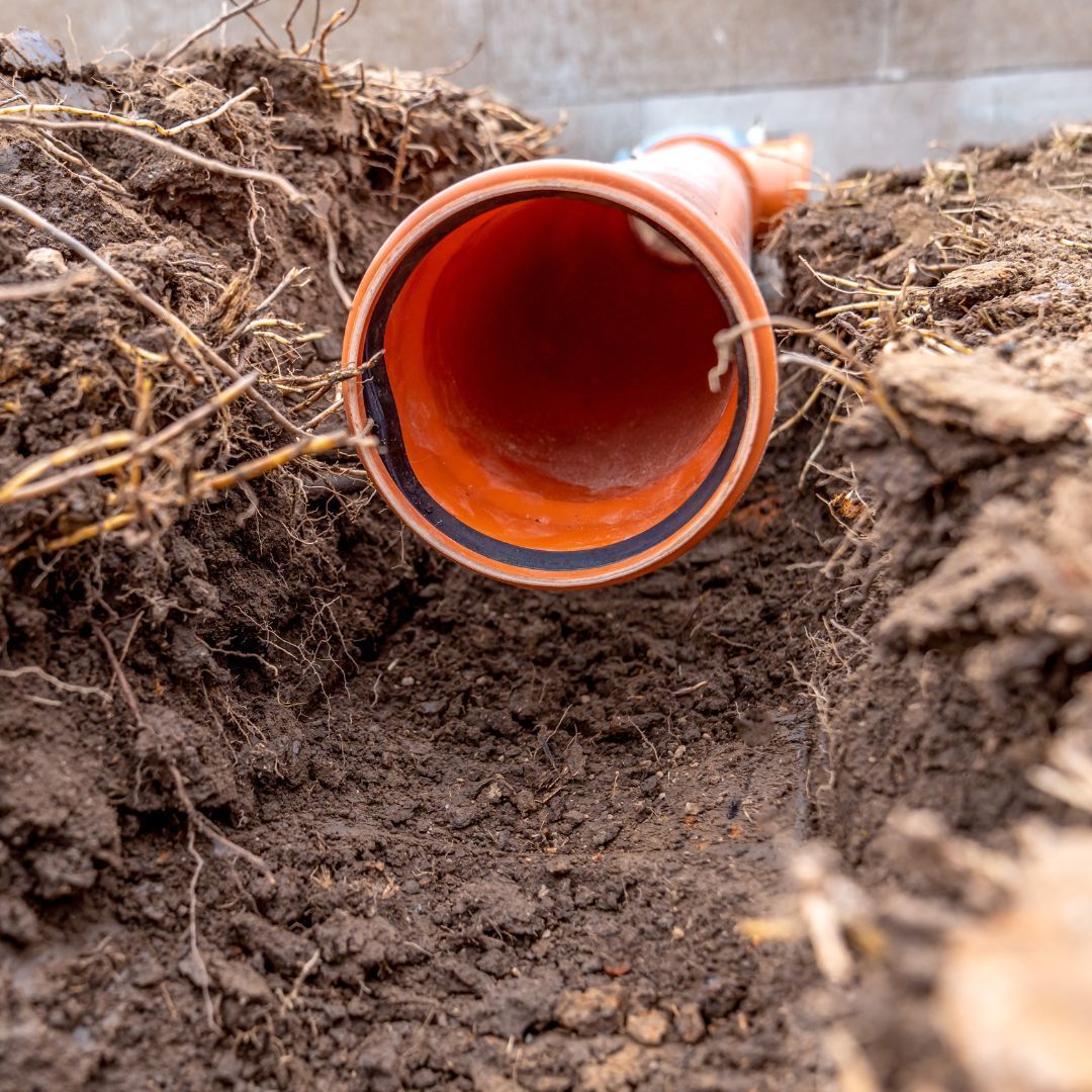 A red pipe is laying in the dirt in a hole.