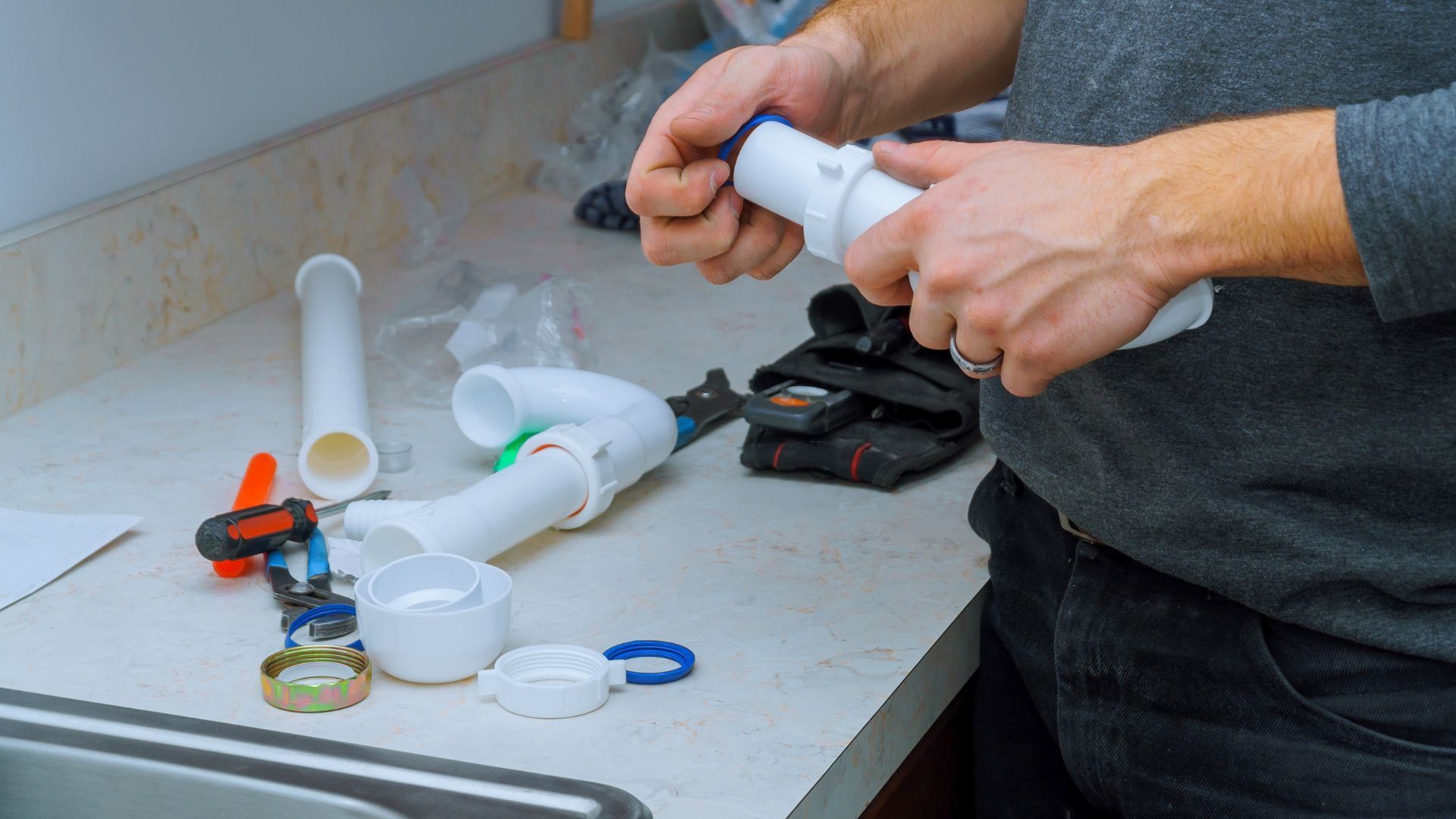 A man is fixing a sink pipe on a counter.