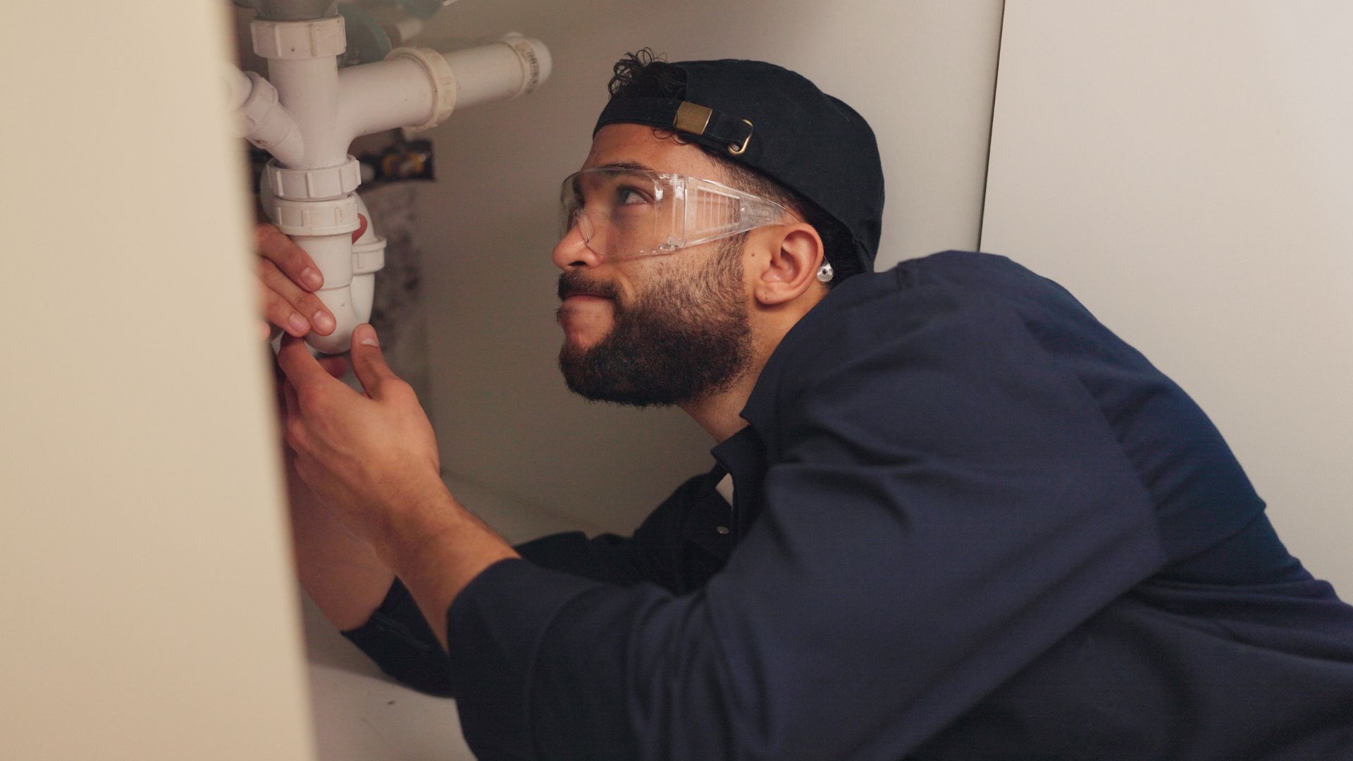 A man is fixing a sink pipe in a bathroom.