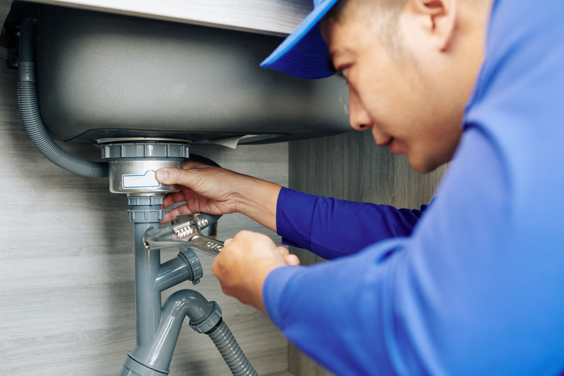 A plumber is fixing a sink with a wrench.