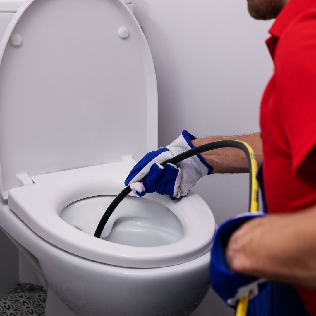 A man in a red shirt is working on a toilet