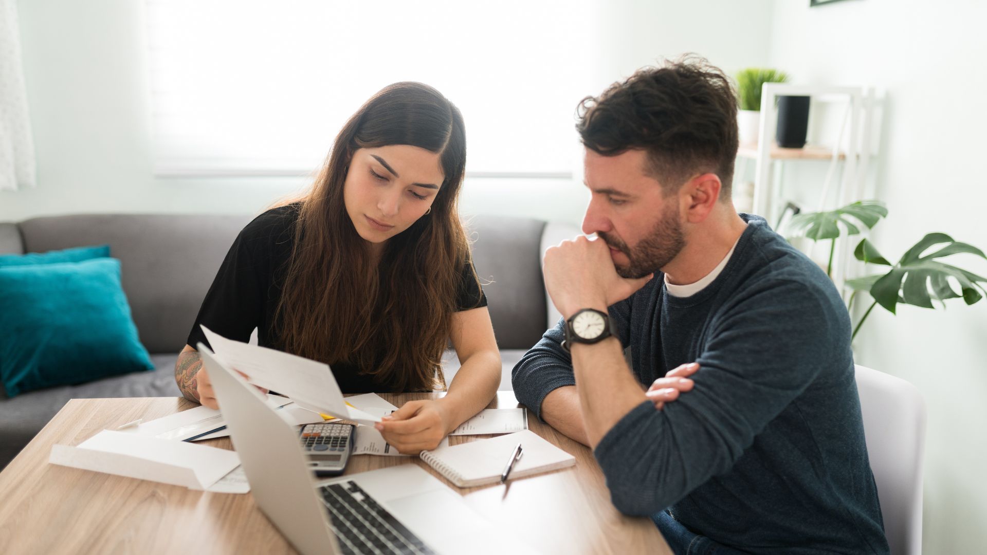 A man and a woman are sitting at a table looking at papers and a laptop.