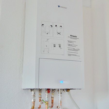A white water heater is hanging on a white wall.
