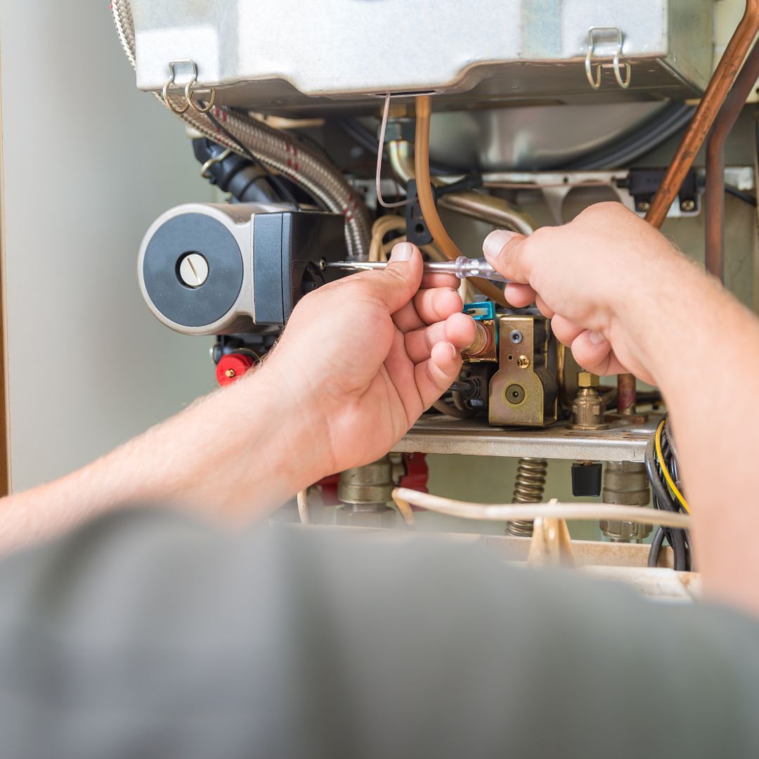 A person is fixing a boiler with a screwdriver.