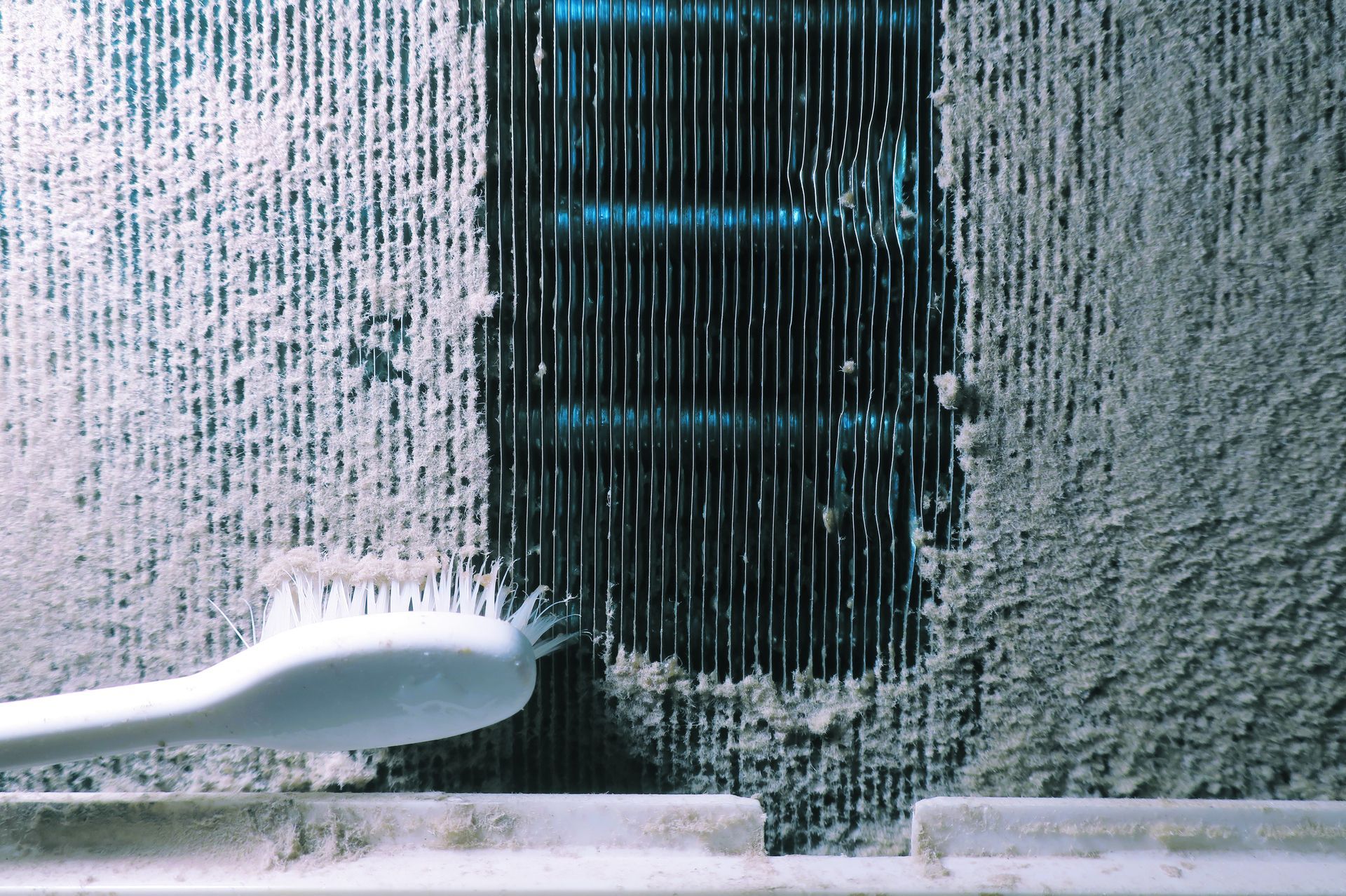 A toothbrush is being used to clean a dirty air conditioner.