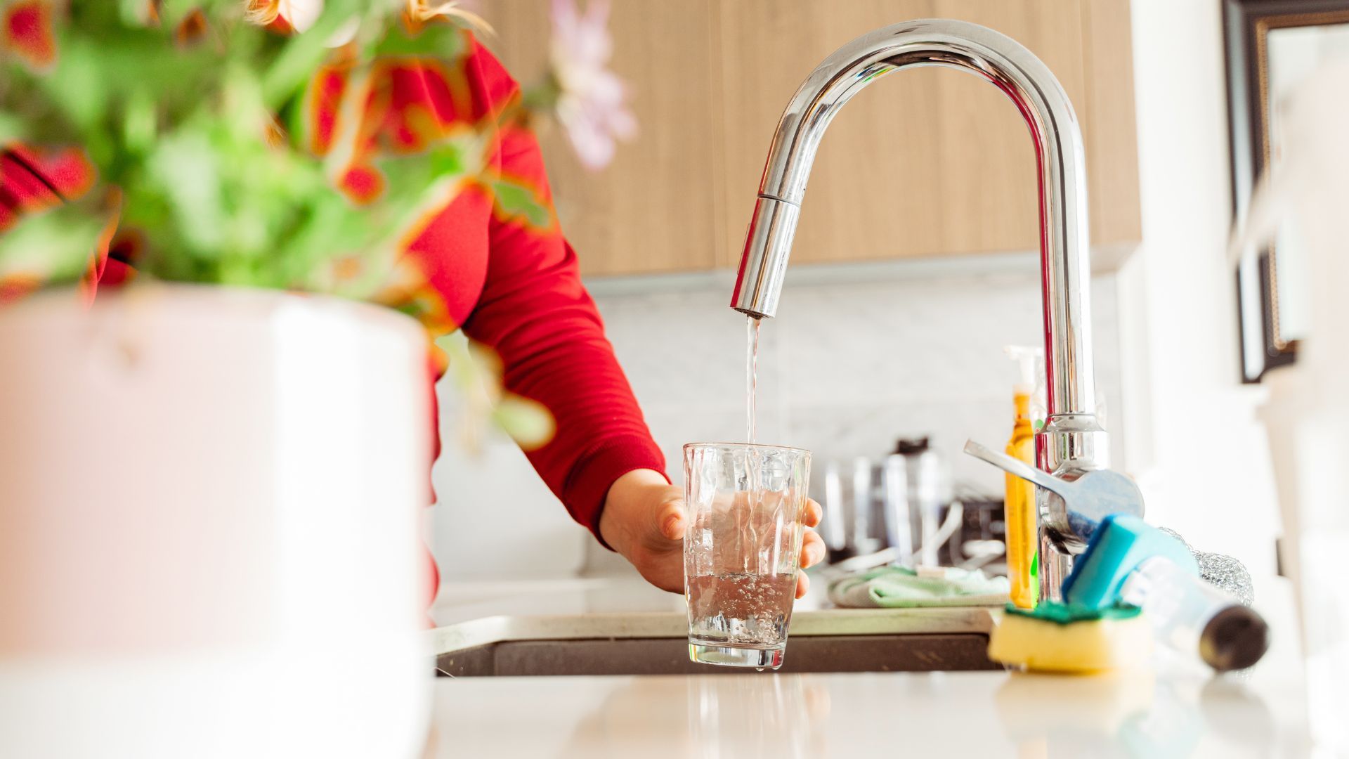 A woman is pouring water into a glass in a kitchen sink.