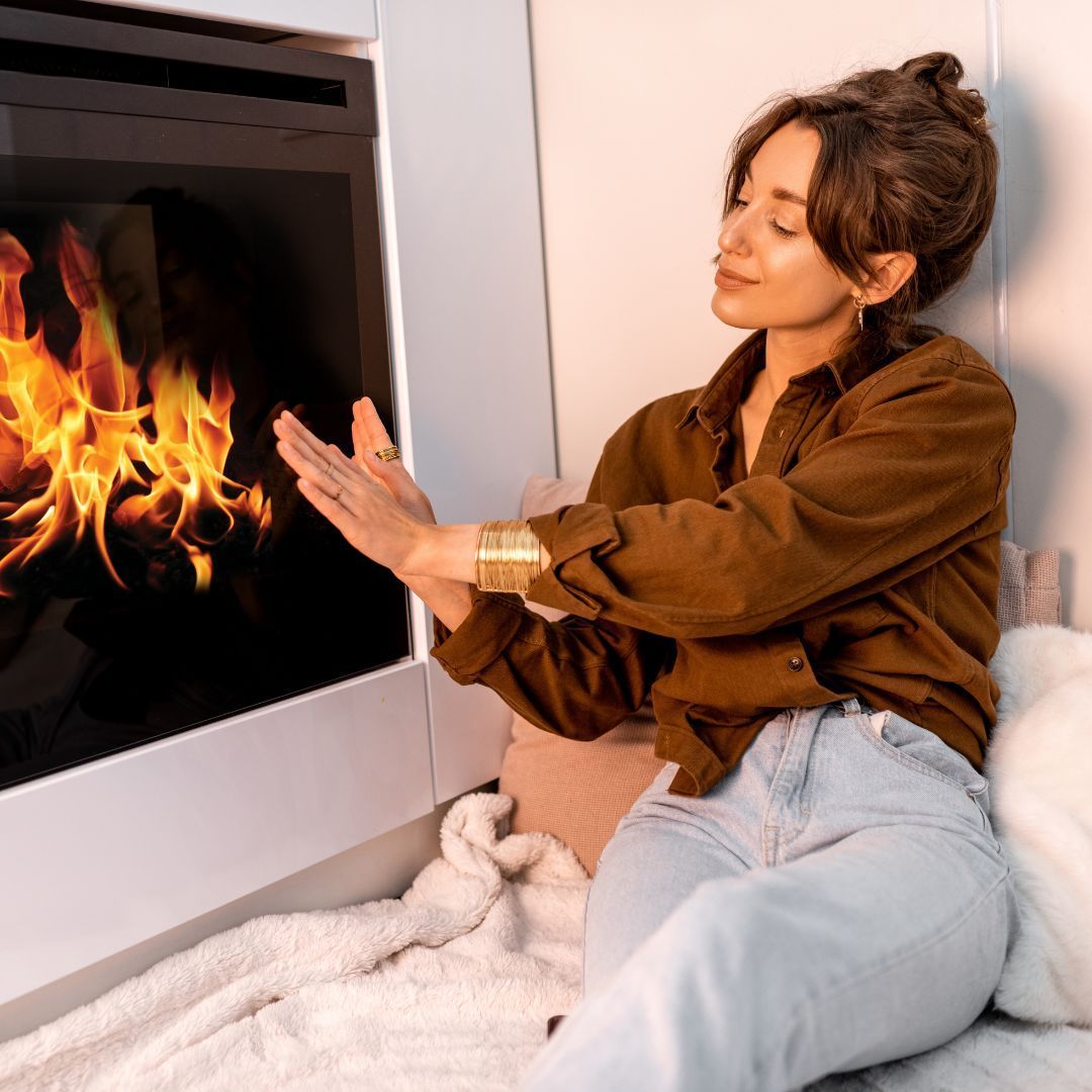 A woman is sitting in front of a fireplace with flames coming out of it.