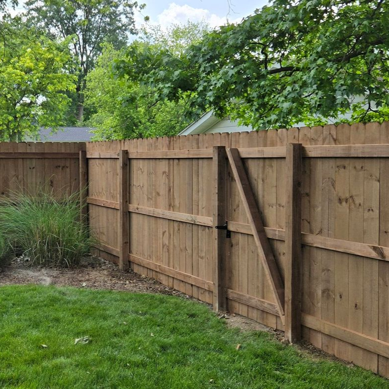 Wooden backyard fence with gate beside green lawn and trees