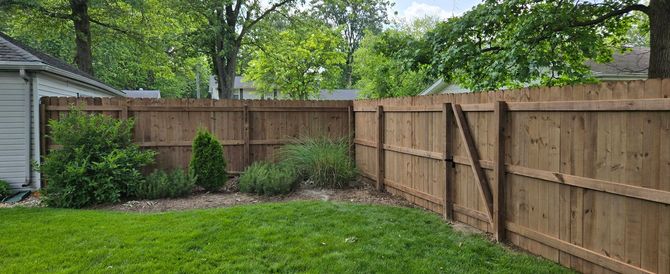 A white vinyl privacy fence encloses a green grassy backyard on a sunny day.