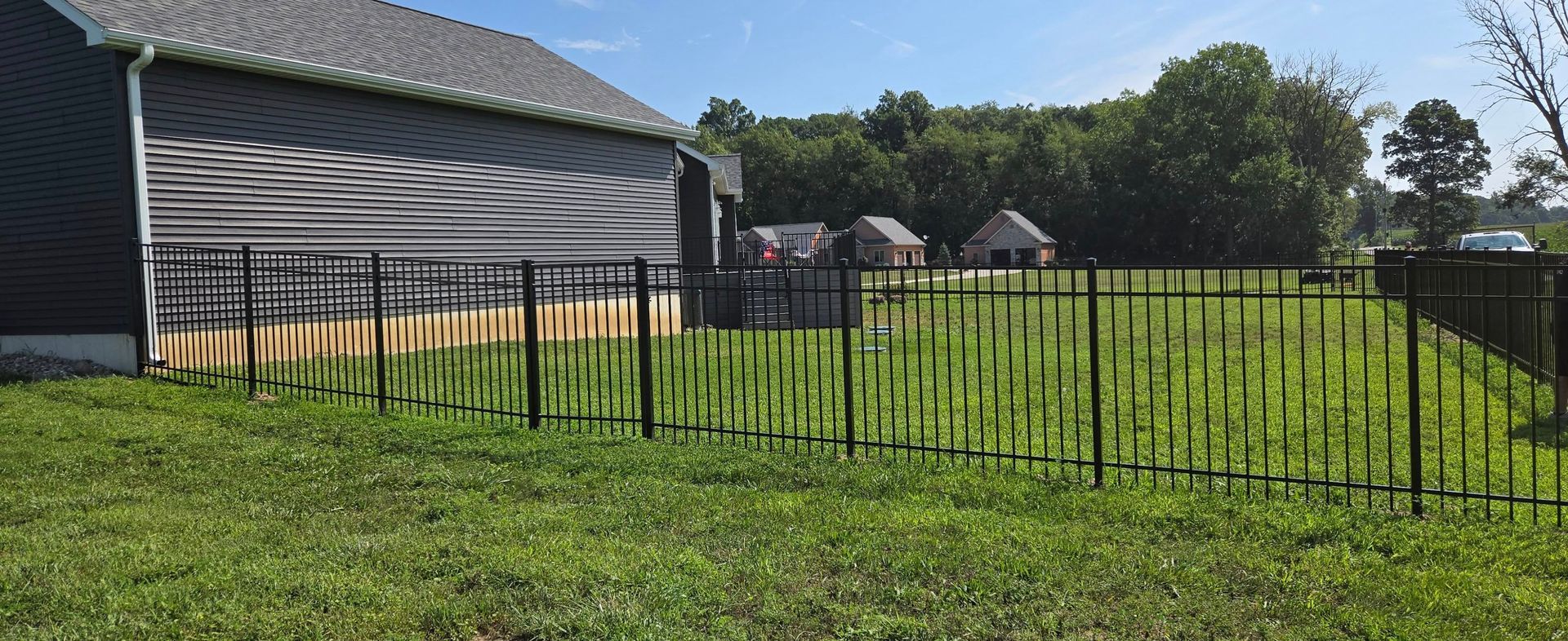 Black metal fence beside a gray house on a sunny grassy lawn