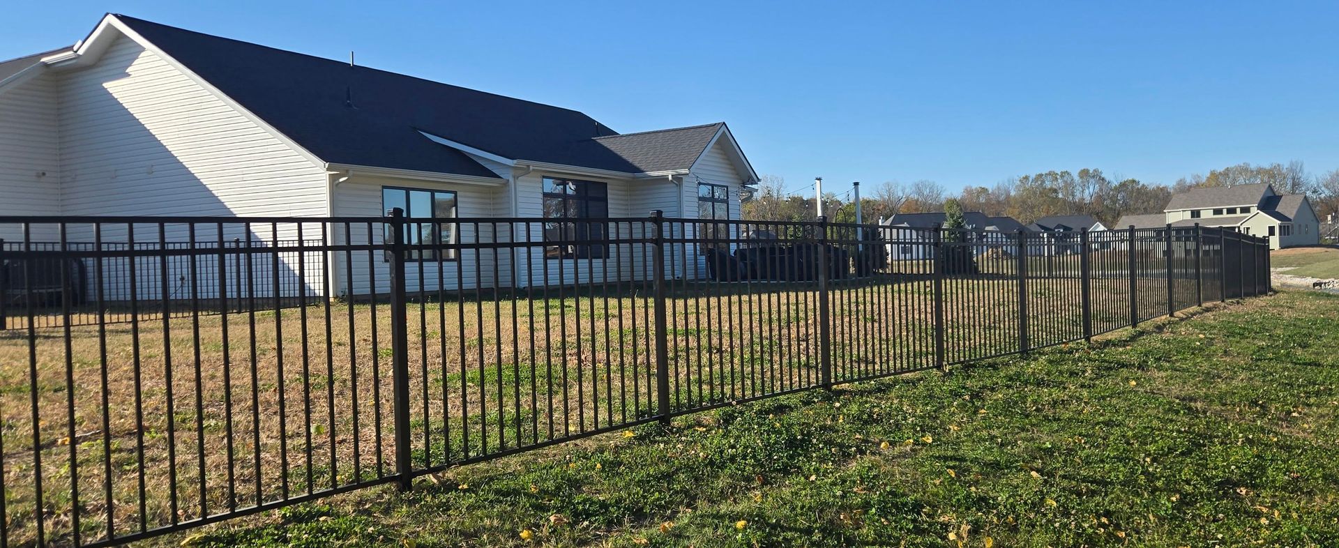 Black metal fence beside white tents on a sunny grassy field under a blue sky
